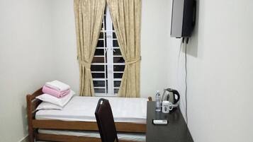 Una habitación pequeña con cama, escritorio, silla, televisión y ventana con cortinas.