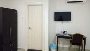 Una habitación con armario, puerta, escritorio con silla, televisor y aire acondicionado.