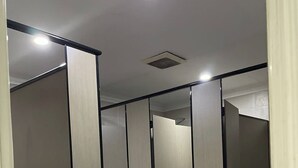 Un pasillo con varios cubículos de baño, cada uno con una puerta espejada y una lámpara arriba.