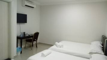 Ein Hotelzimmer mit zwei Einzelbetten, einem Schreibtisch mit Stuhl, einem an der Wand befestigten Flachbildfernseher und einer Klimaanlage.