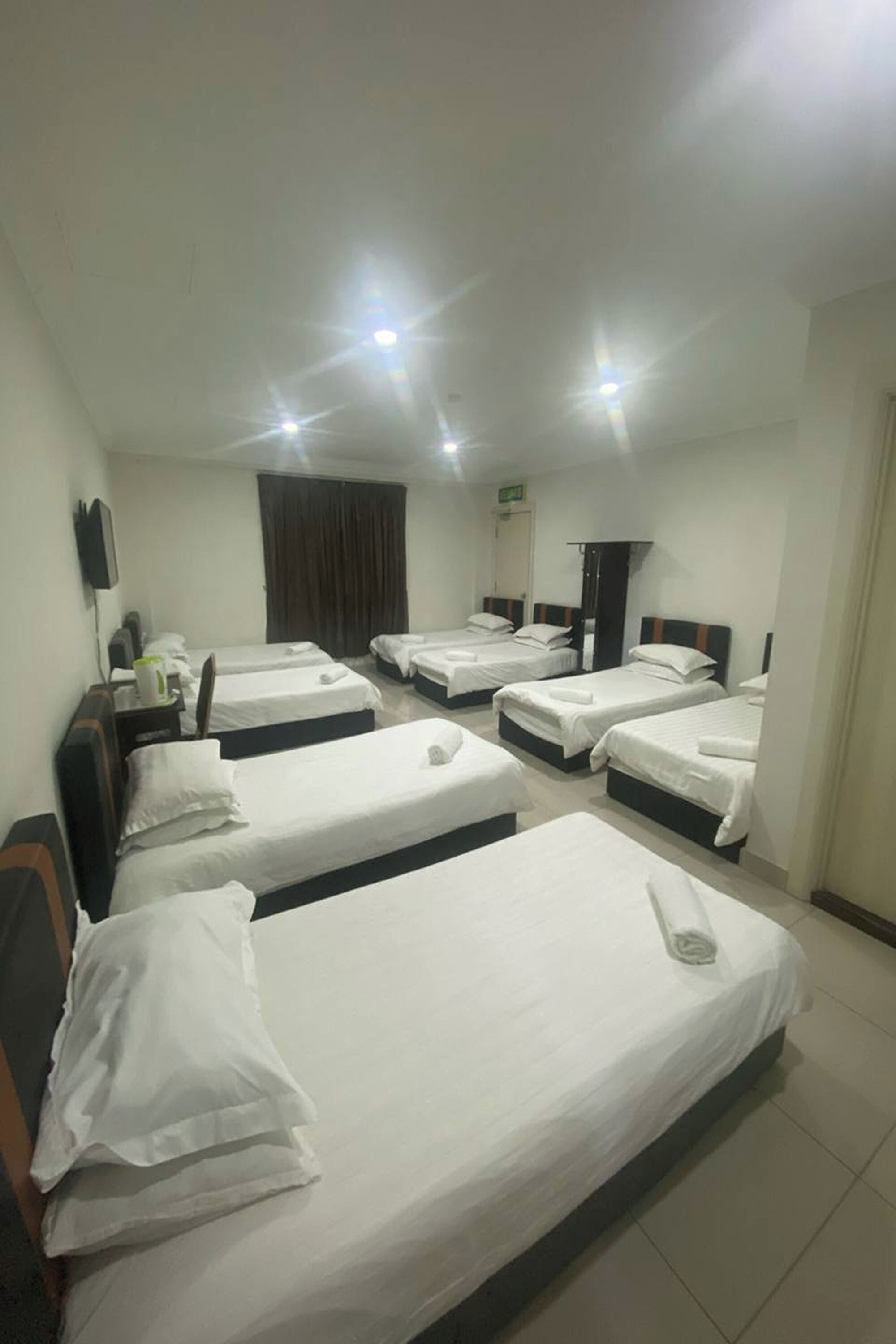 A hotel room with four single beds, a flat-screen TV on the wall, and a mirror.