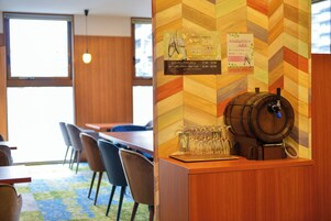Zona de bar con mostrador de madera, grifo de cerveza y cartel con la carta. Se observan sillas y mesas al fondo.