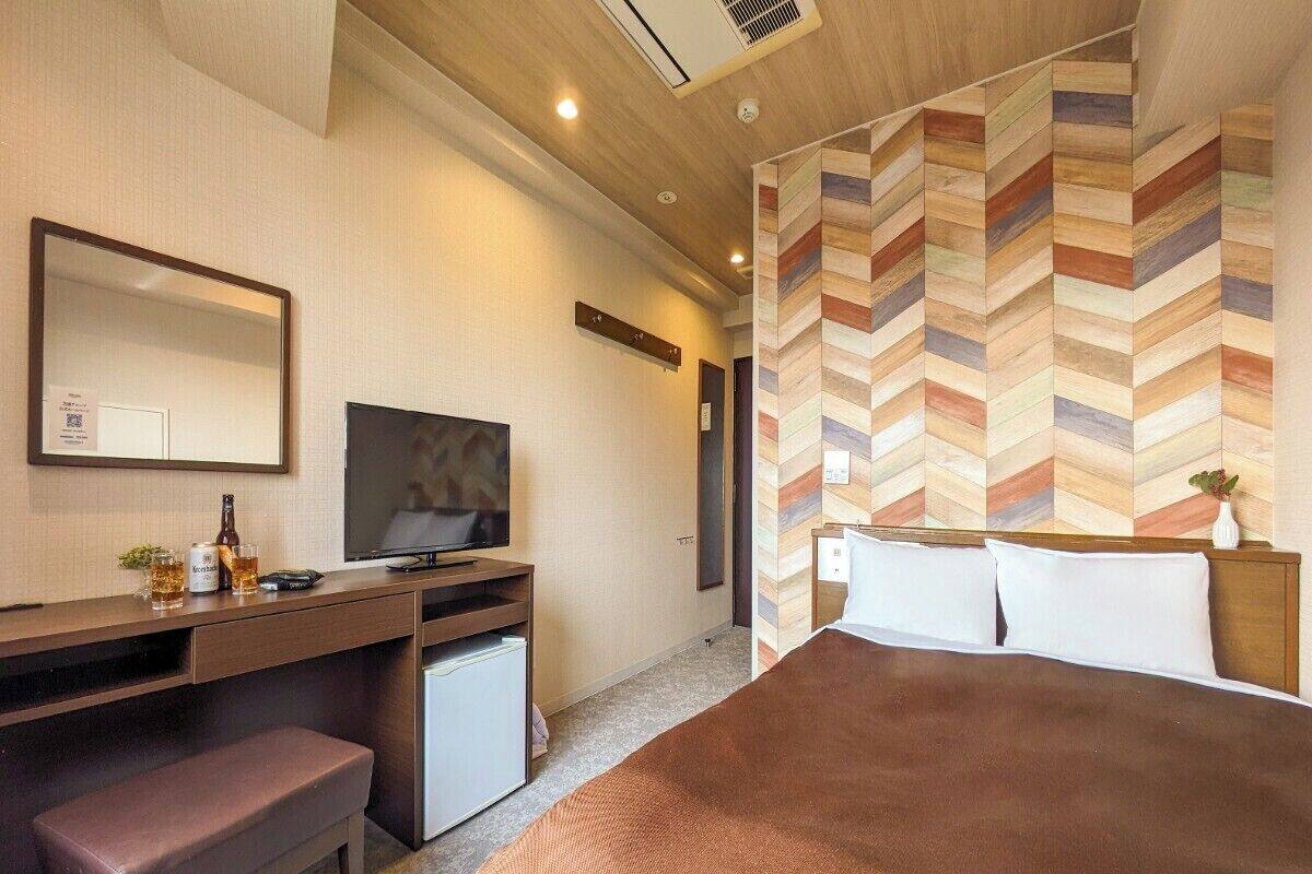 A hotel room with a bed, a desk with a computer, a television, and a small seating area.
