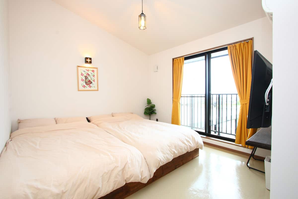 A bedroom with a bed, a plant, a TV, and a window with curtains.