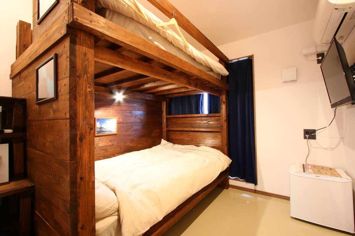 A wooden bunk bed with a headboard, a bedside table, and a small window with curtains.