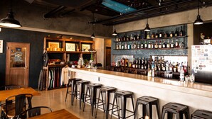 Zona de bar con una barra larga, varios taburetes y estantes llenos de botellas.