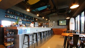 Una zona de bar con mostrador, taburetes y una decoración con una tabla de surf.