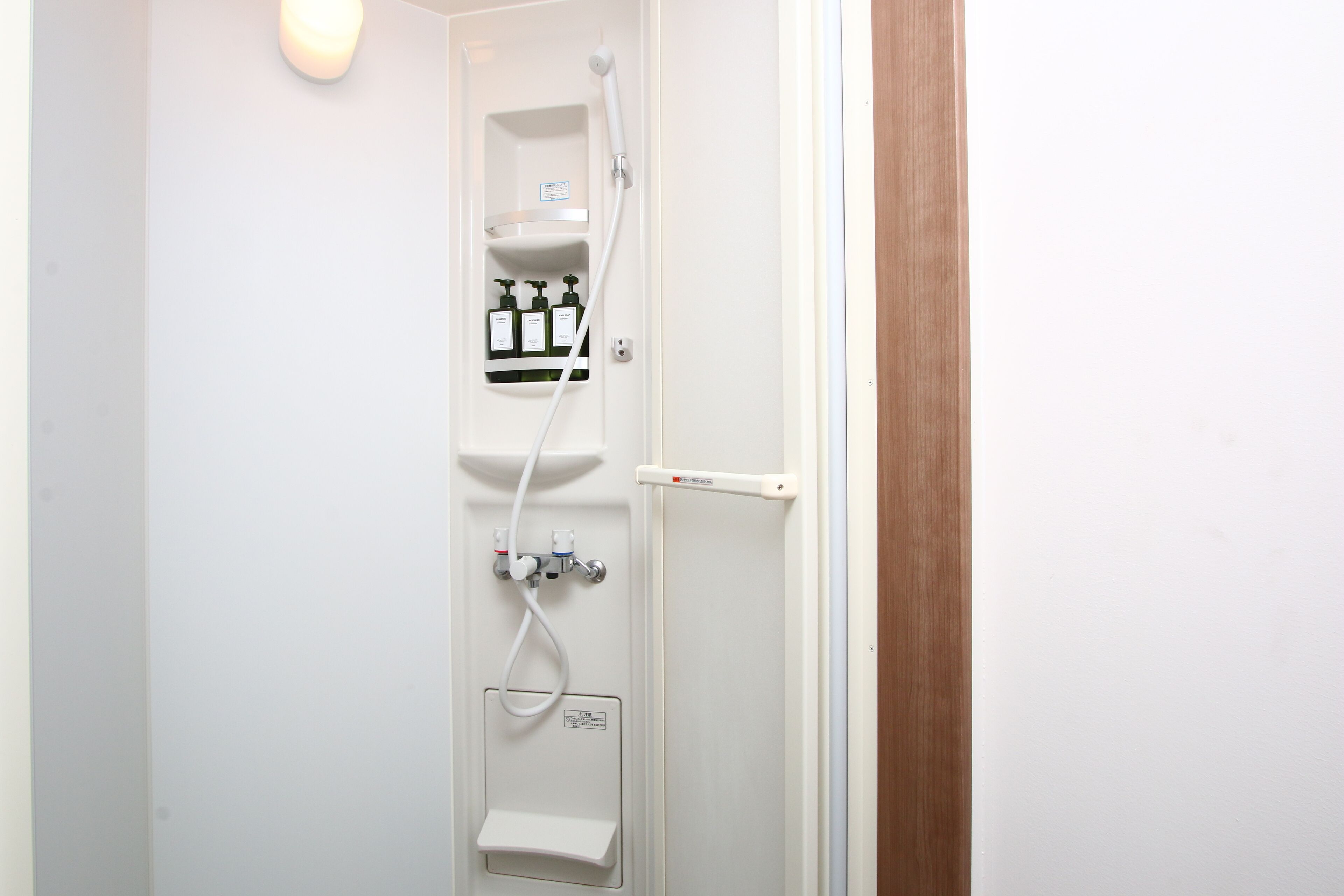 Box de chuveiro branco com chuveiro manual, dispensador de sabonete e painel de controle.