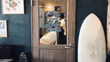 Eine Tür, in einem Spiegel darin sichtbar: ein Friseursalon, ein Surfbrett und ein gemustertes Handtuch.