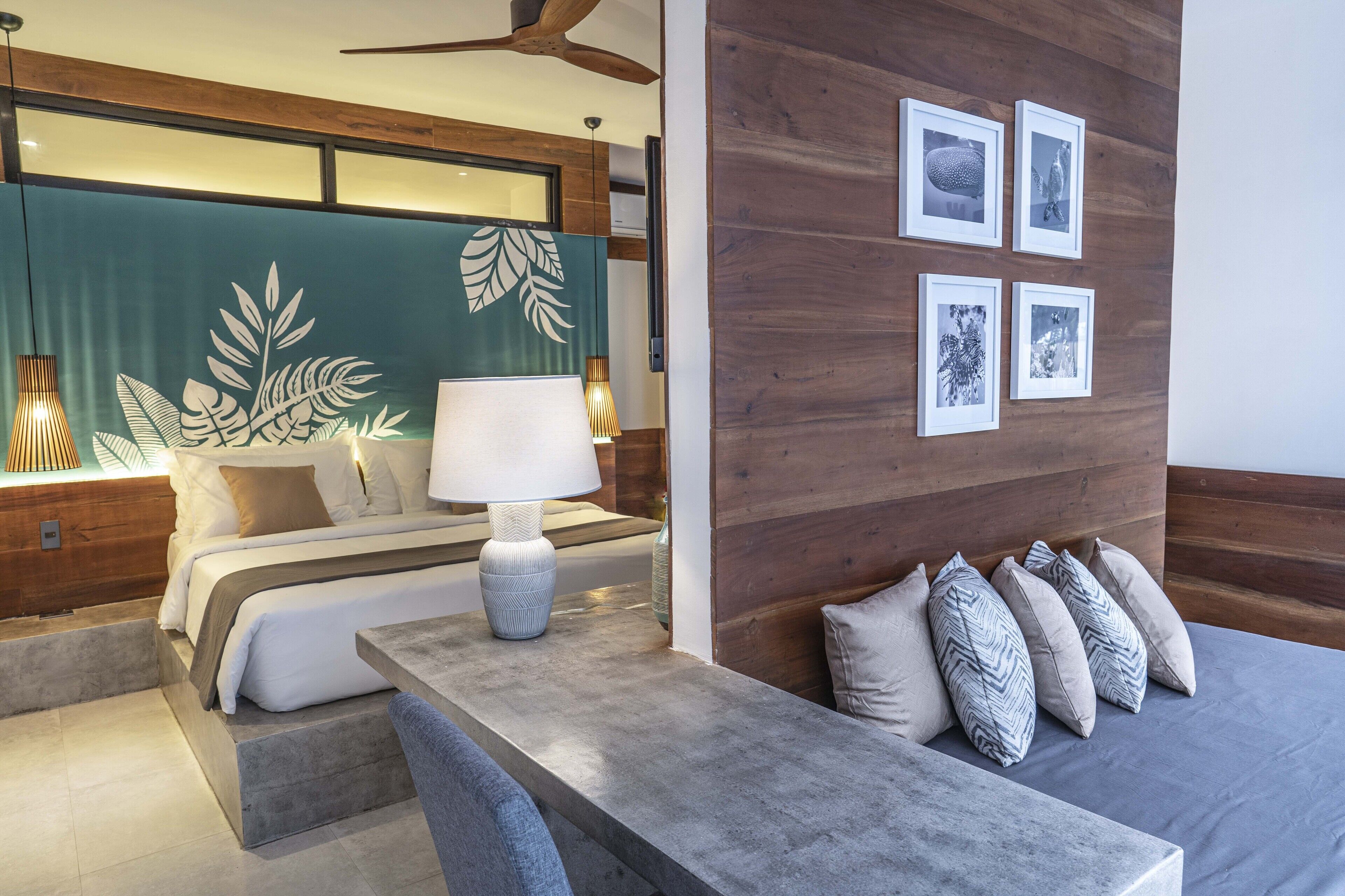 Een moderne hotelkamer met een bed, een bureau, een lamp en een muur met ingelijste foto's.
