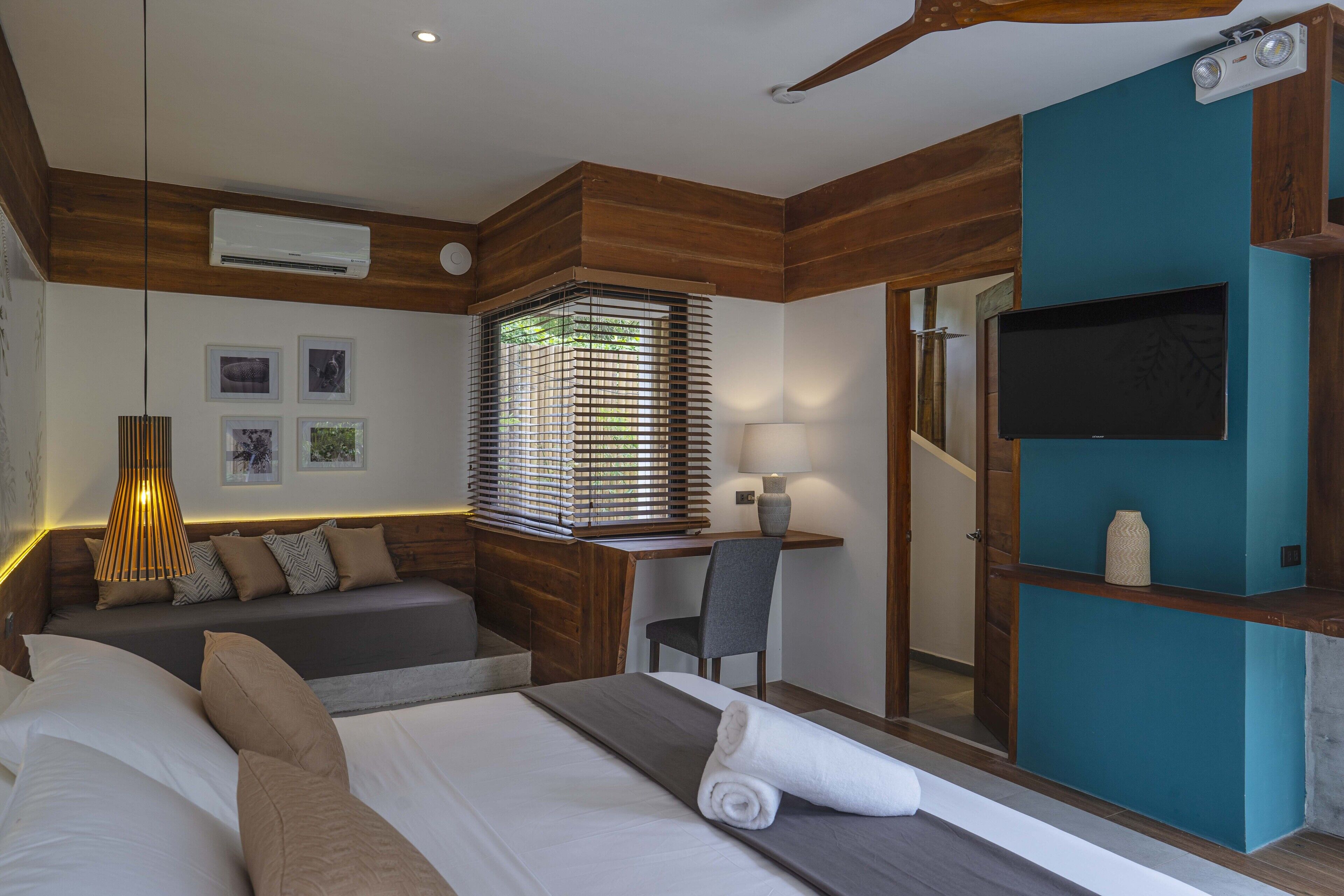 A modern hotel room with a bed, a desk, a chair, a TV, and a window with blinds.