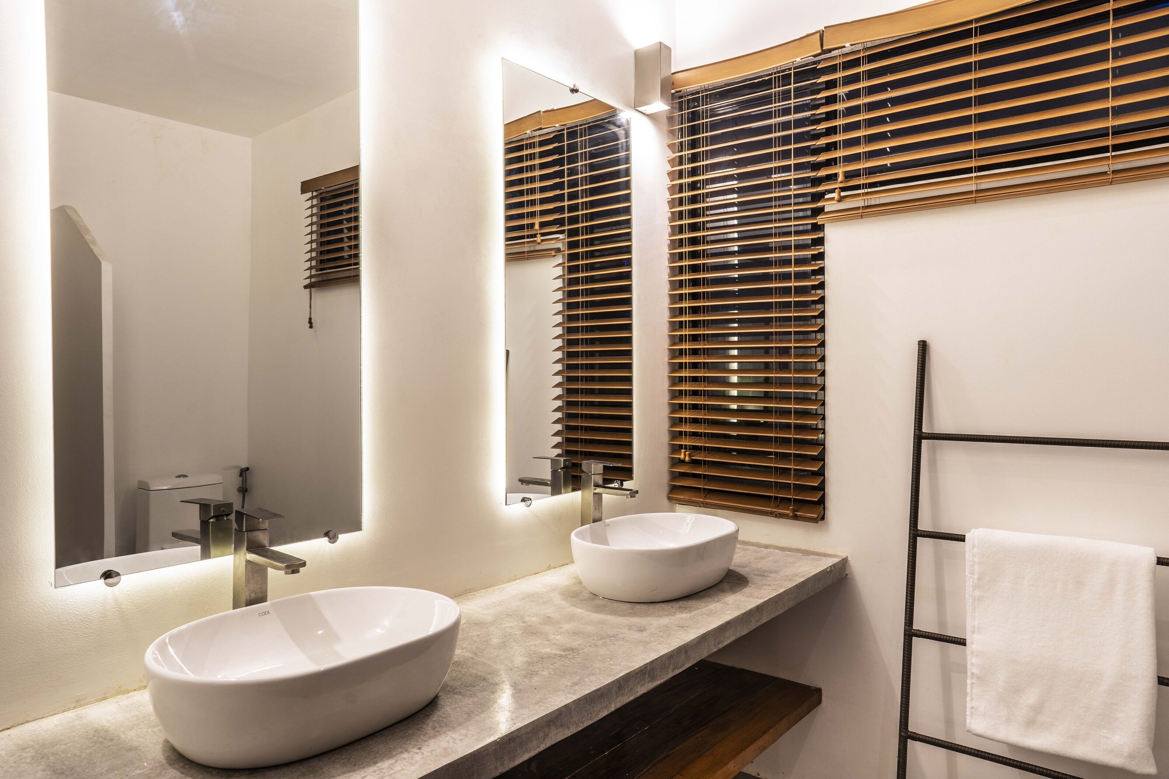 Une salle de bain moderne avec deux vasques, un grand miroir et des stores en bois.