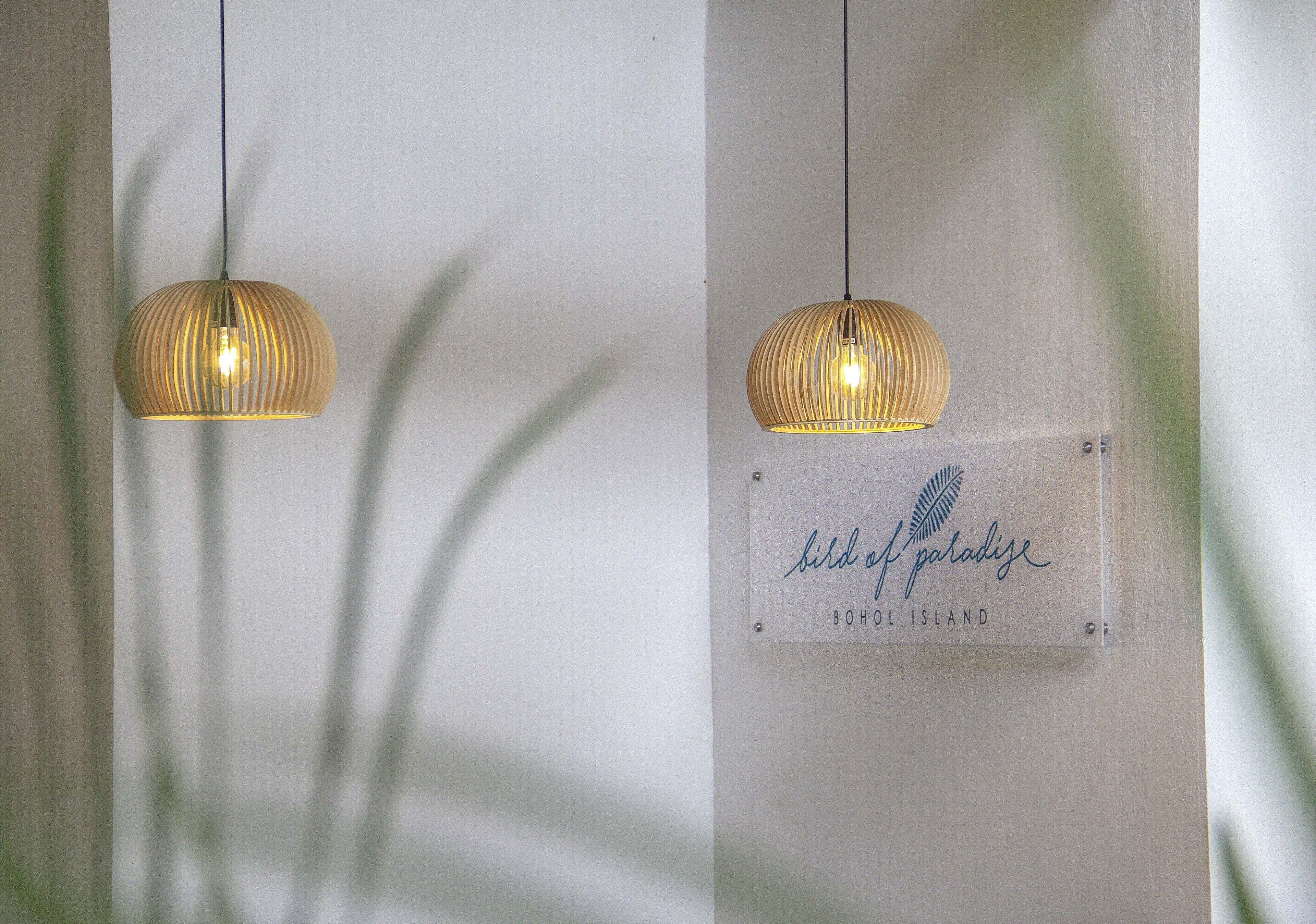 Two hanging pendant lights with a ribbed design, a sign with the text "bird of paradise" and "BOHOL ISLAND" on a wall.