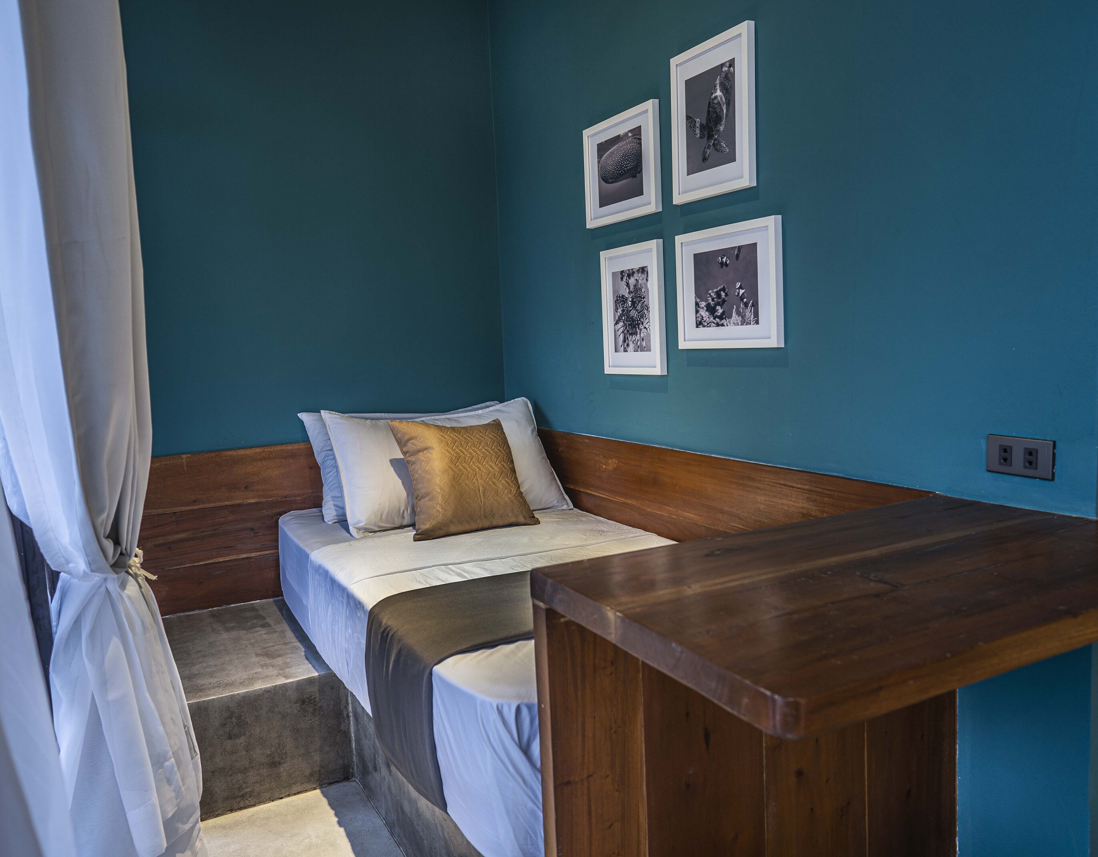 A small, cozy room with a bed, a wooden bench, and a wall with framed pictures.