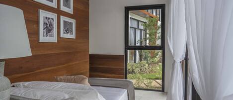 A bedroom with a bed, a bedside table, a lamp, and a window with curtains.