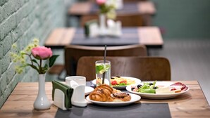 Una mesa de comedor con un croissant, una ensalada en un plato, un vaso de agua con pajita, y un florero con flores.
