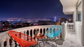Un balcón con dos sillas y una mesa, con vista a un paisaje urbano nocturno.