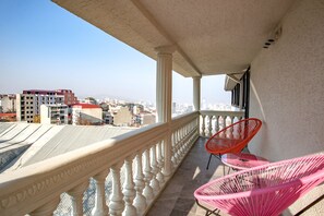 Un balcón con barandilla blanca, dos sillas rosas y vistas de la ciudad.