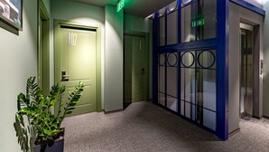 Un pasillo con una puerta verde con el número 402, un ascensor con marco azul y una planta en maceta.