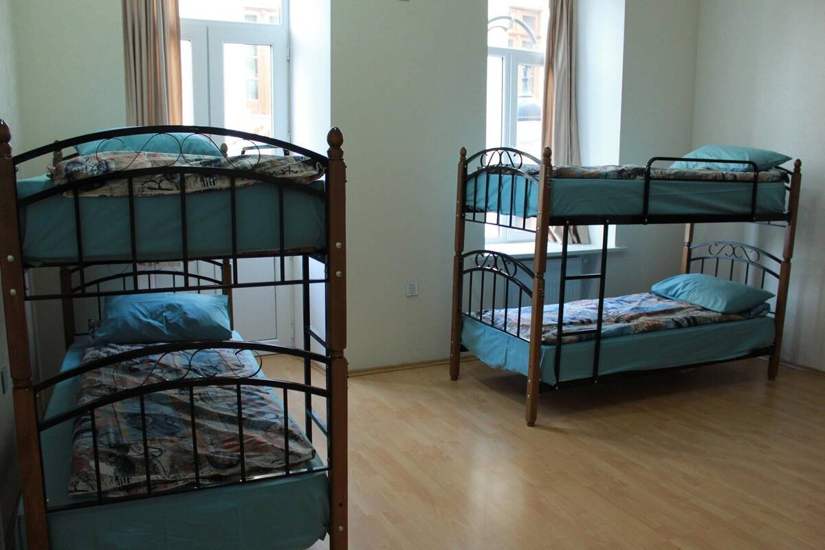 A room with three bunk beds, wooden flooring, and a window with curtains.