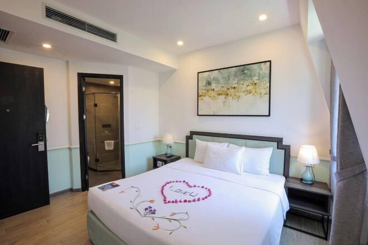 A hotel room with a bed, a nightstand, a wall-mounted painting, and a door.