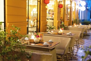 Un restaurante con mobiliario de mimbre y mesas dispuestas para comer, con un expositor de menú y flores decorativas.