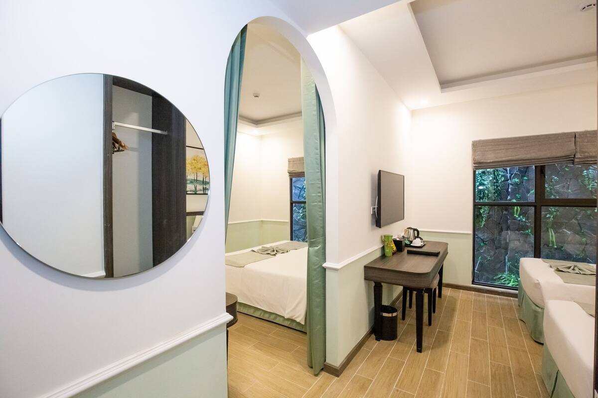 A modern hotel room with a bed, a desk, and a window with a view of greenery.
