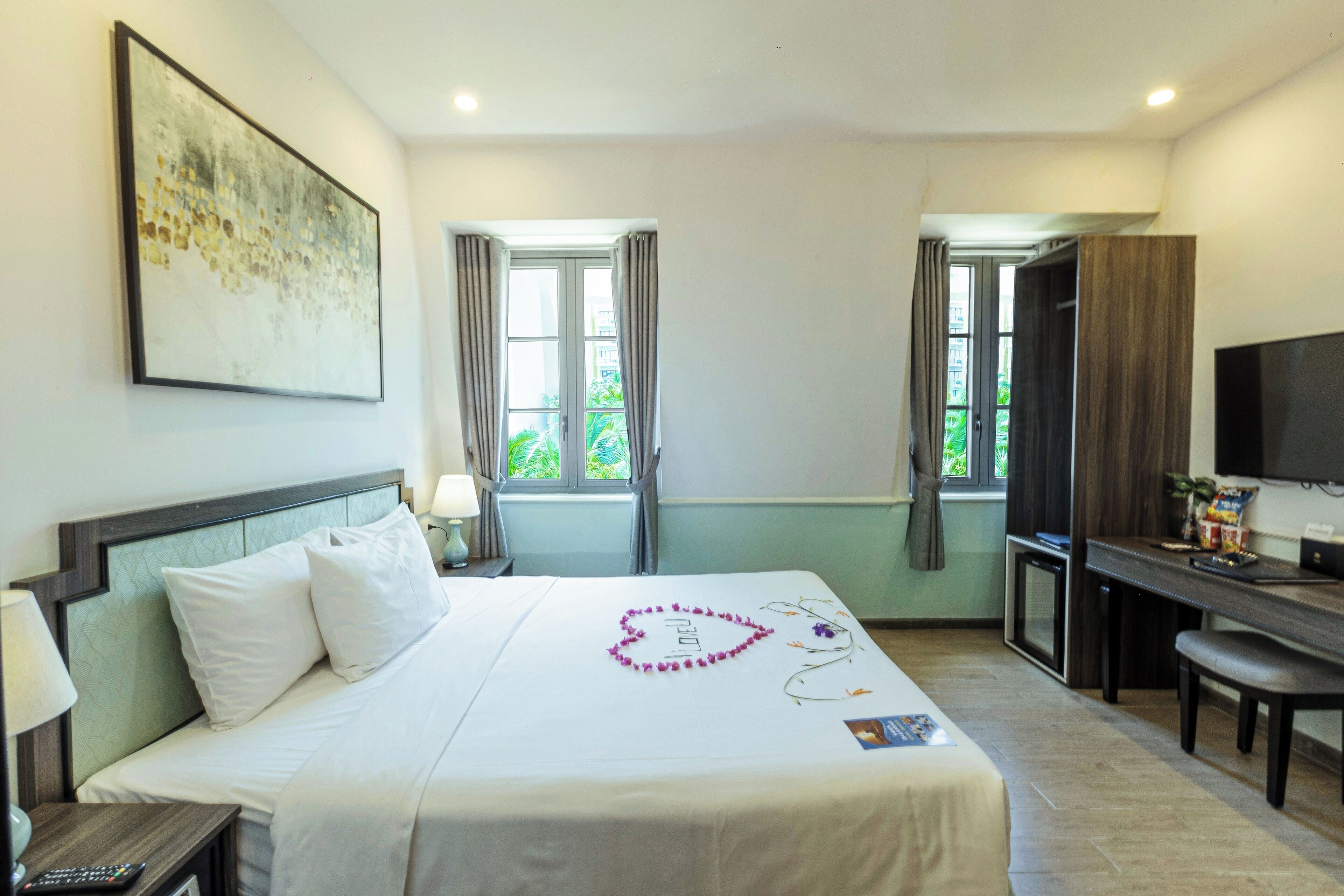 Quarto de hotel com cama, escrivaninha, televisão e janela com cortinas.