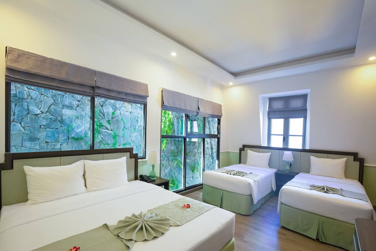 A hotel room with two beds, a stone wall, and a window with a view of greenery.