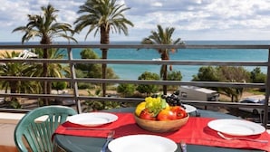 Mesa para dos con frutero, platos y cubiertos en un balcón con vista al mar.
