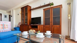 Una sala de estar con una mesa de centro de vidrio, sofá azul, armarios de madera y un televisor de pantalla plana.