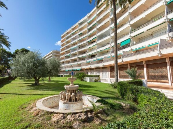 A multi-story hotel with balconies, a central courtyard with a fountain, and surrounding greenery. - Apartment Gregal by Interhome (Miami Platja)