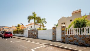 A gated residential area with a white fence, stone walls, and a red car parked on the street. - Stunning Villa Mila in Madroñal, heated pool! (Adeje)