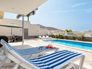 A poolside area with lounge chairs, a table, and an umbrella.