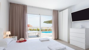 A hotel room with a bed, a TV, a desk with a lamp, and a view of a swimming pool. - Stunning Villa Mila in Madroñal, heated pool! (Adeje)
