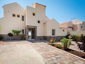 A modern building with a stone facade, a central entrance, and a paved courtyard with plants.