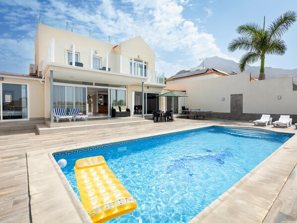 A modern house with a swimming pool, outdoor seating, and a palm tree.