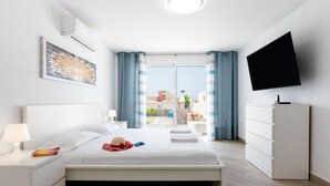 A modern hotel room with a large bed, a flat-screen TV, a desk with a lamp, and a view of the city. - Stunning Villa Mila in Madroñal, heated pool! (Adeje)