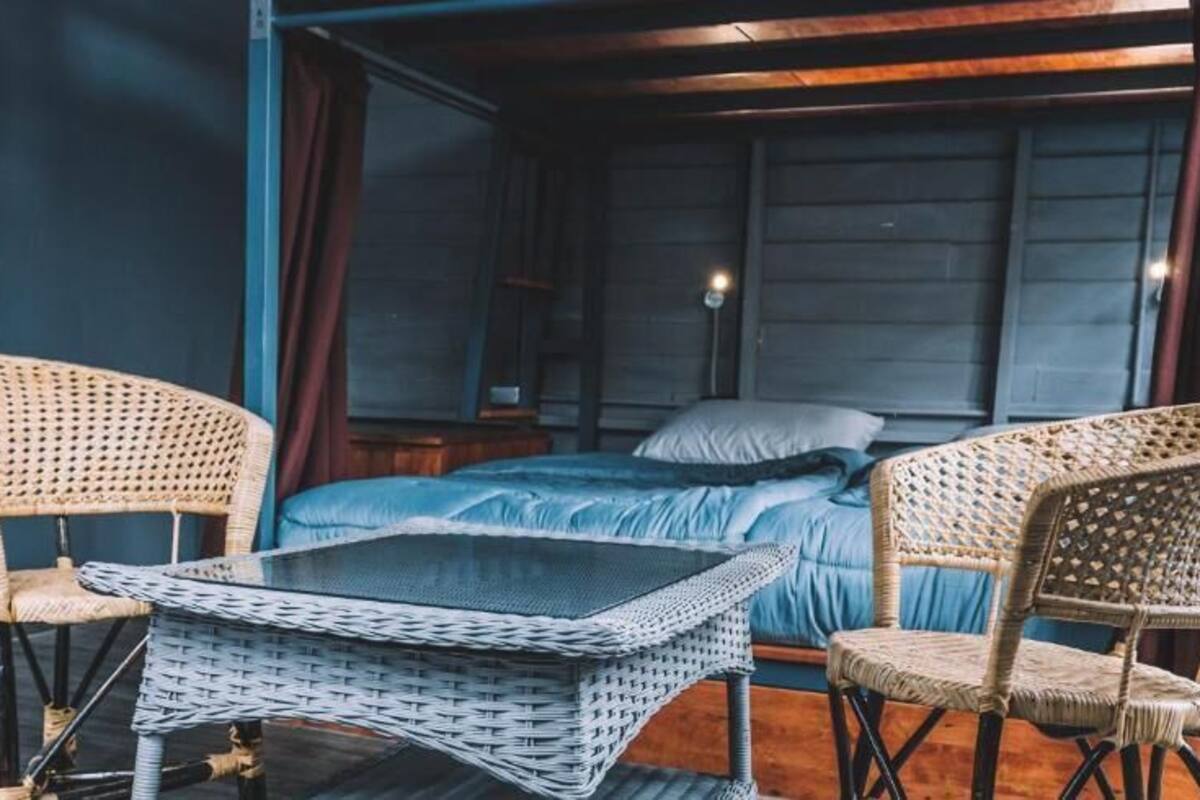 A room with a bed, two wicker chairs, a small table, and a nightstand.