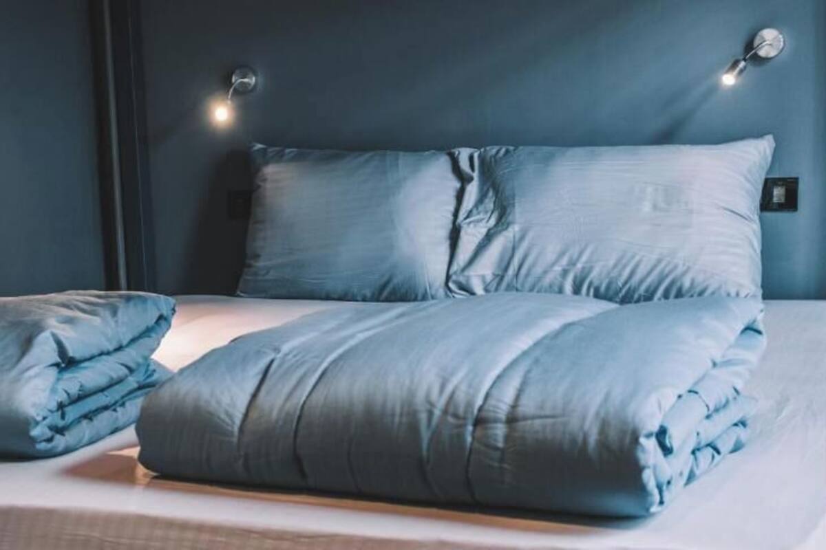 A bed with a blue blanket and pillows, a bedside lamp, and a wall-mounted light fixture.