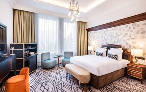 A hotel room with a large bed, a desk with a chair, a small round table, and a bench. - The Merchant Baku (Baku)