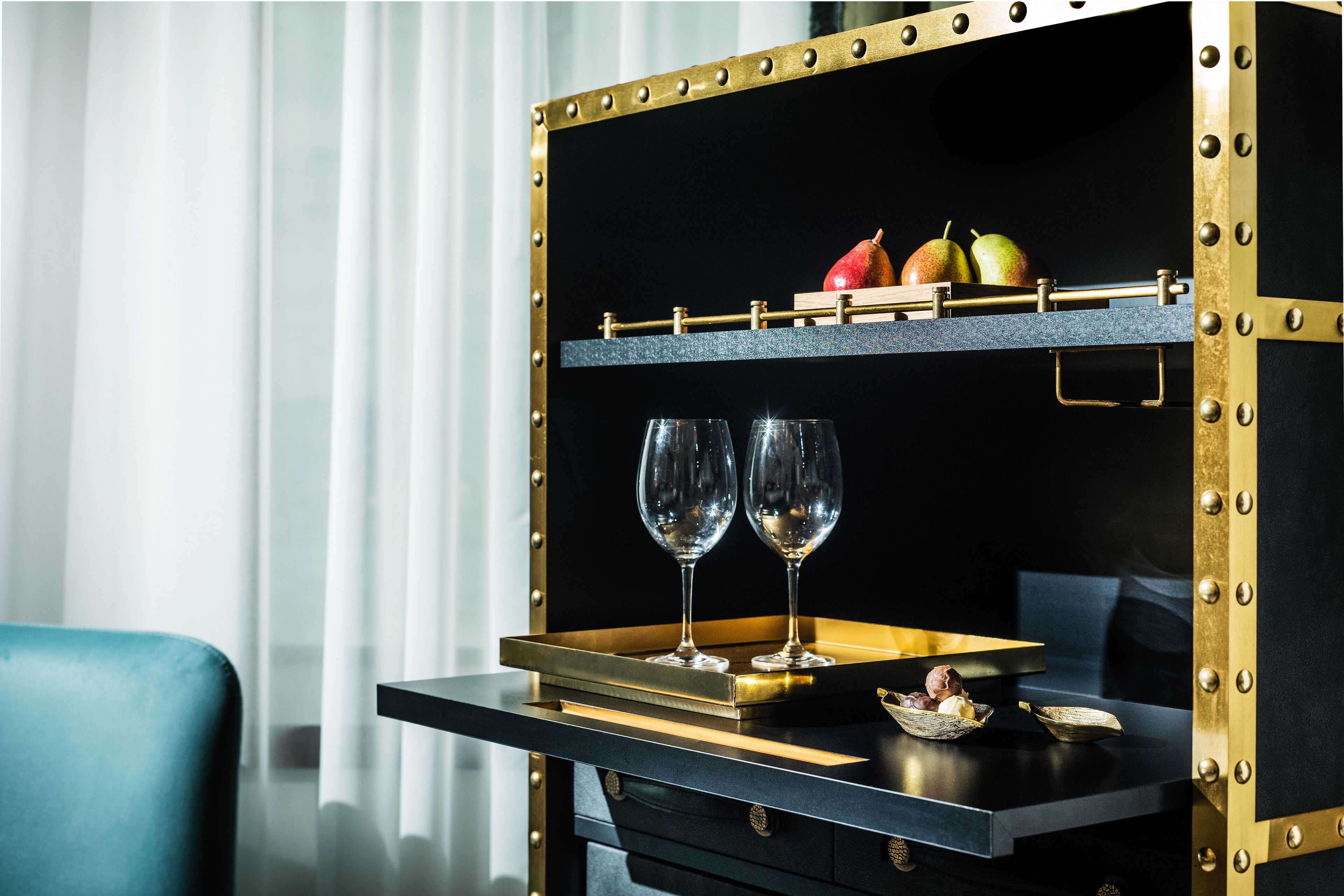 A black and gold minibar with two wine glasses and a fruit tray.