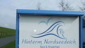 Letrero de 'Hinterm Nordseedich Bed & Breakfast' con un logotipo que presenta olas estilizadas.