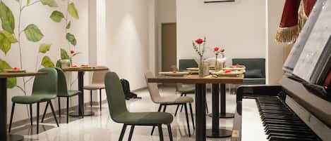 A dining area with a piano, green chairs, and a wall with leaf patterns.