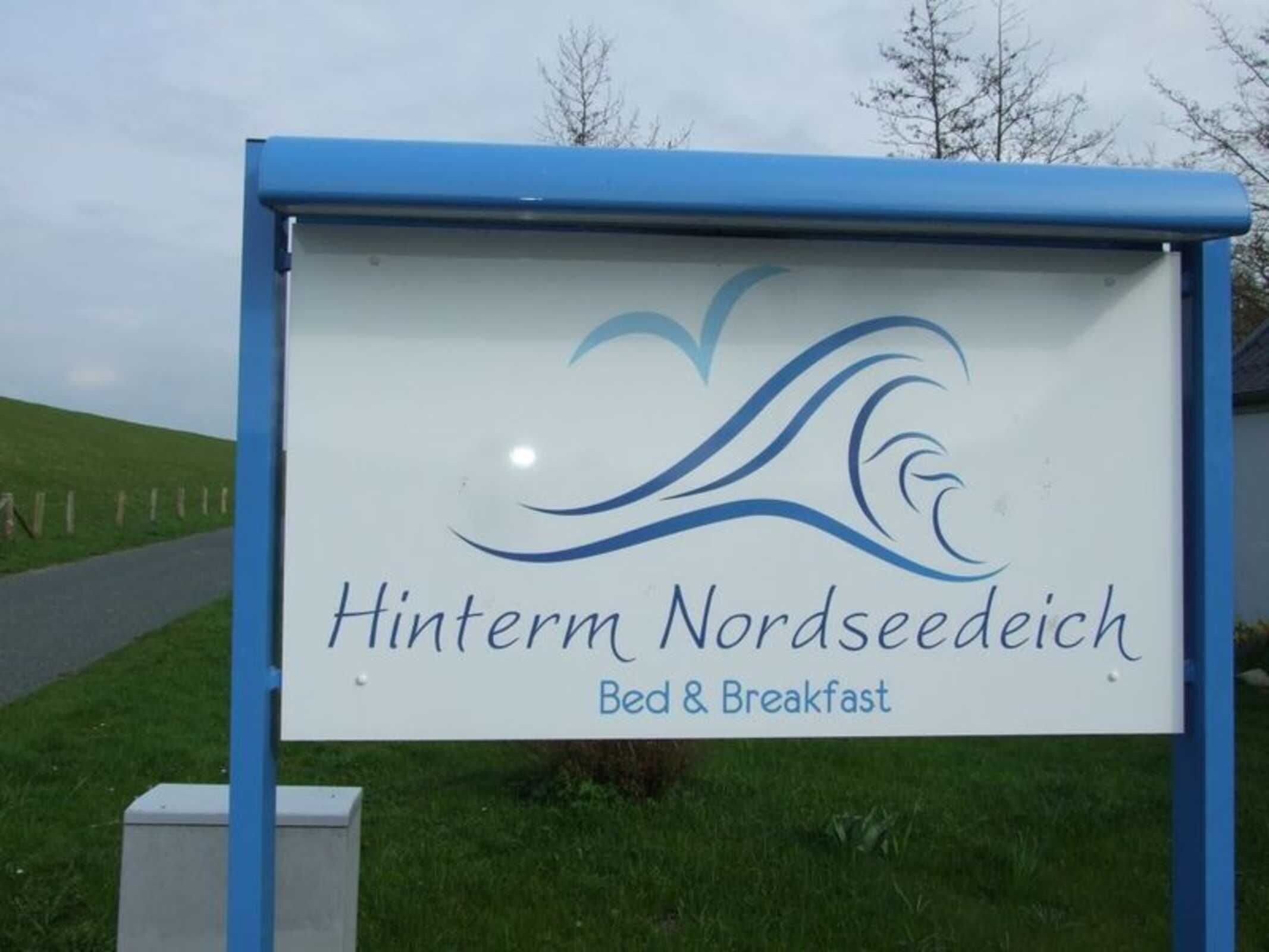 A sign for 'Hinterm Nordseedich Bed & Breakfast' with a logo featuring stylized waves.