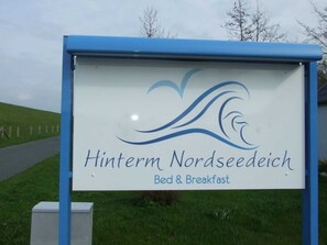 Une enseigne pour le «Hinterm Nordseedich Bed & Breakfast», avec un logo représentant des vagues stylisées.