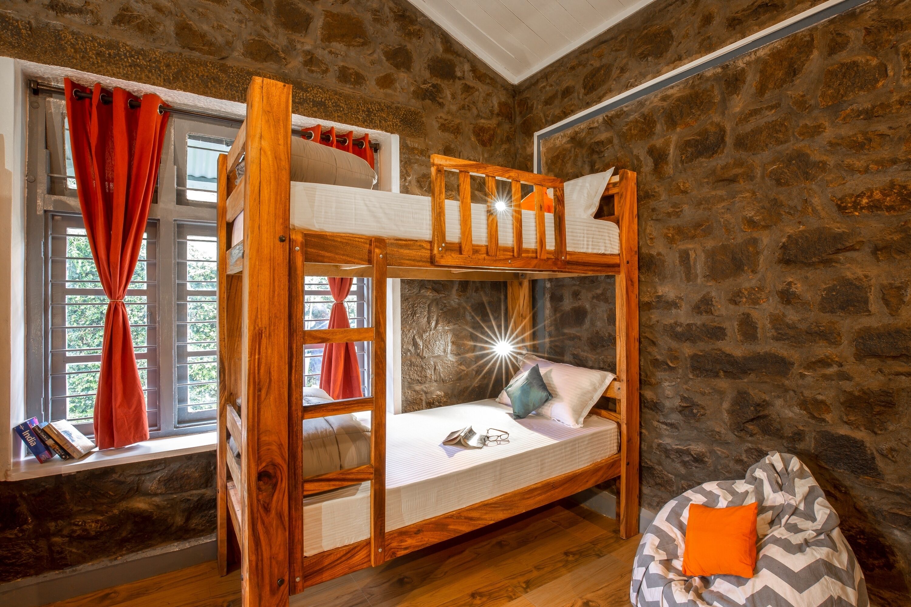 Une chambre avec un lit superposé, un mur en pierre, une fenêtre avec des rideaux et un fauteuil en forme de sac de haricots.