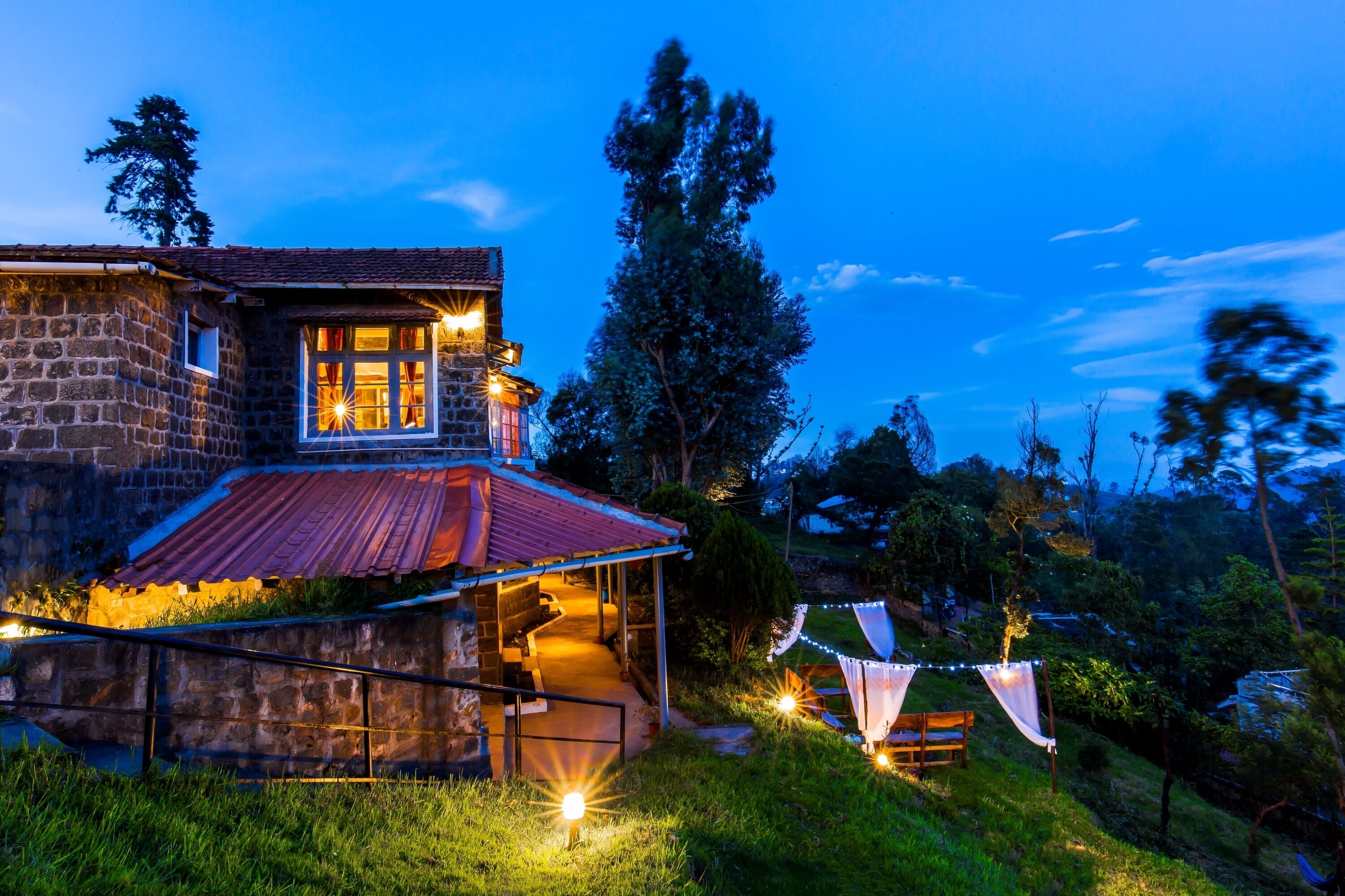 A stone house with a red roof, a porch, and string lights.