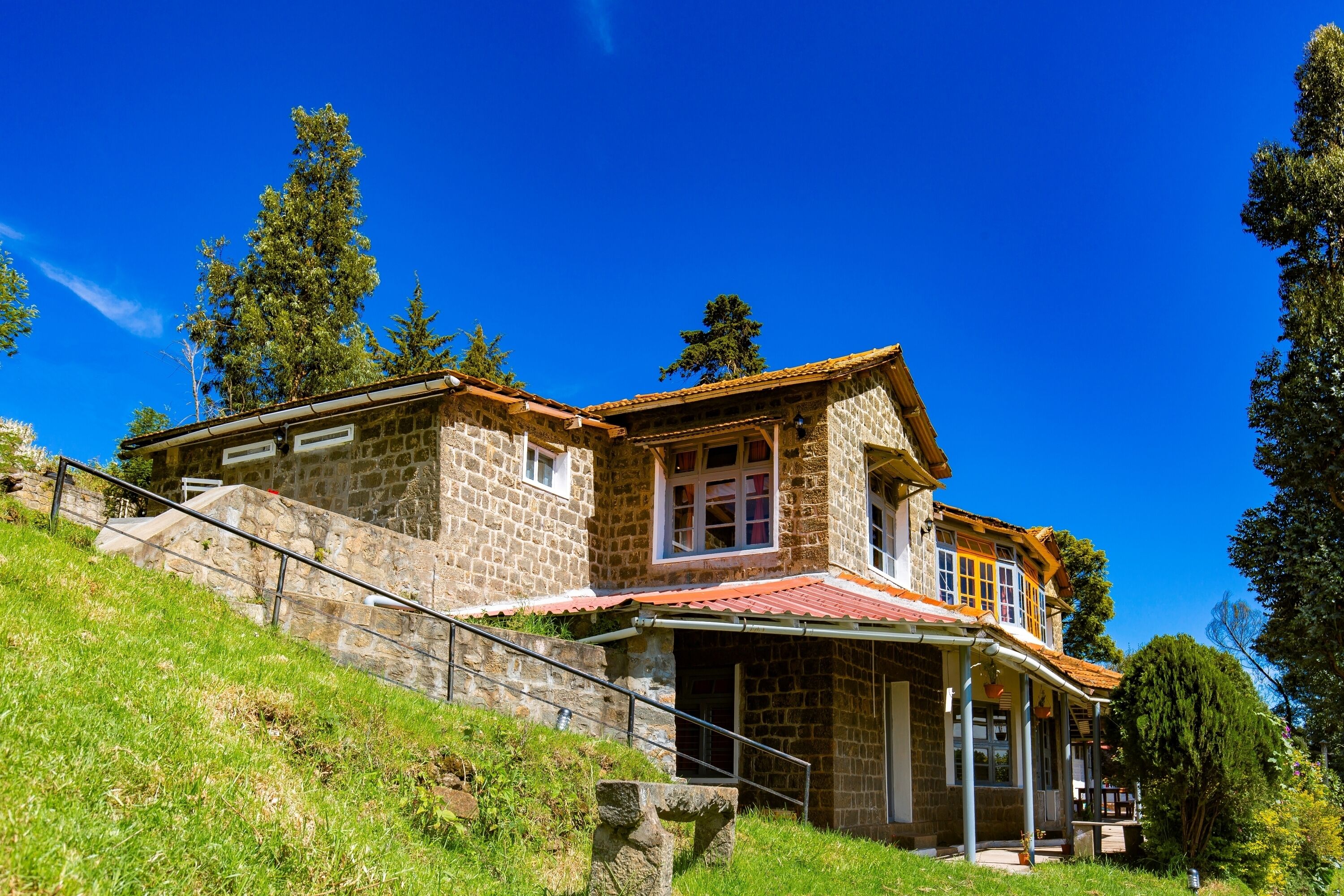 A stone house with a red-tiled roof, a stone staircase, and a grassy hillside.