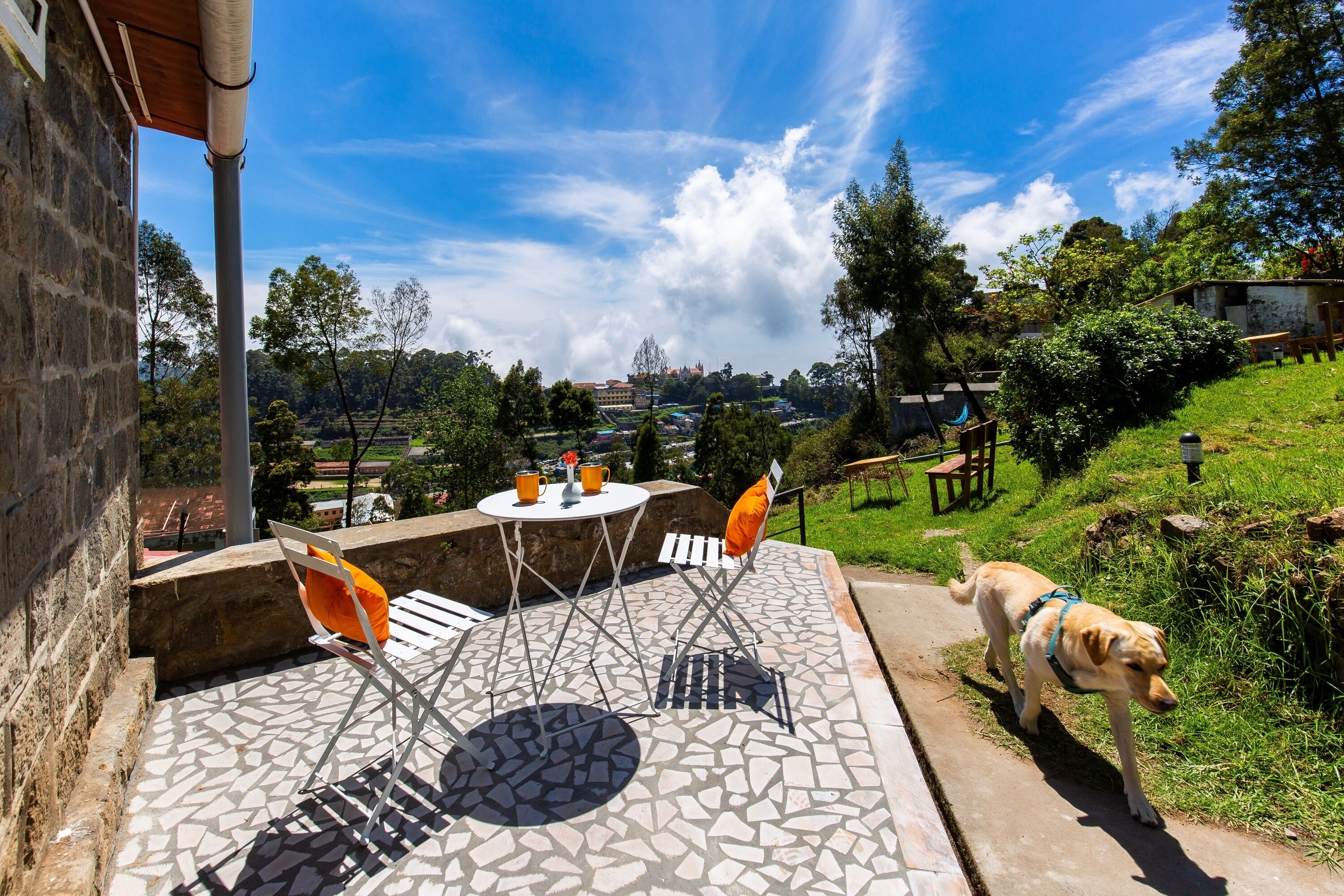 An outdoor patio with a stone-tiled floor, metal chairs, and a table with a cup and saucer.